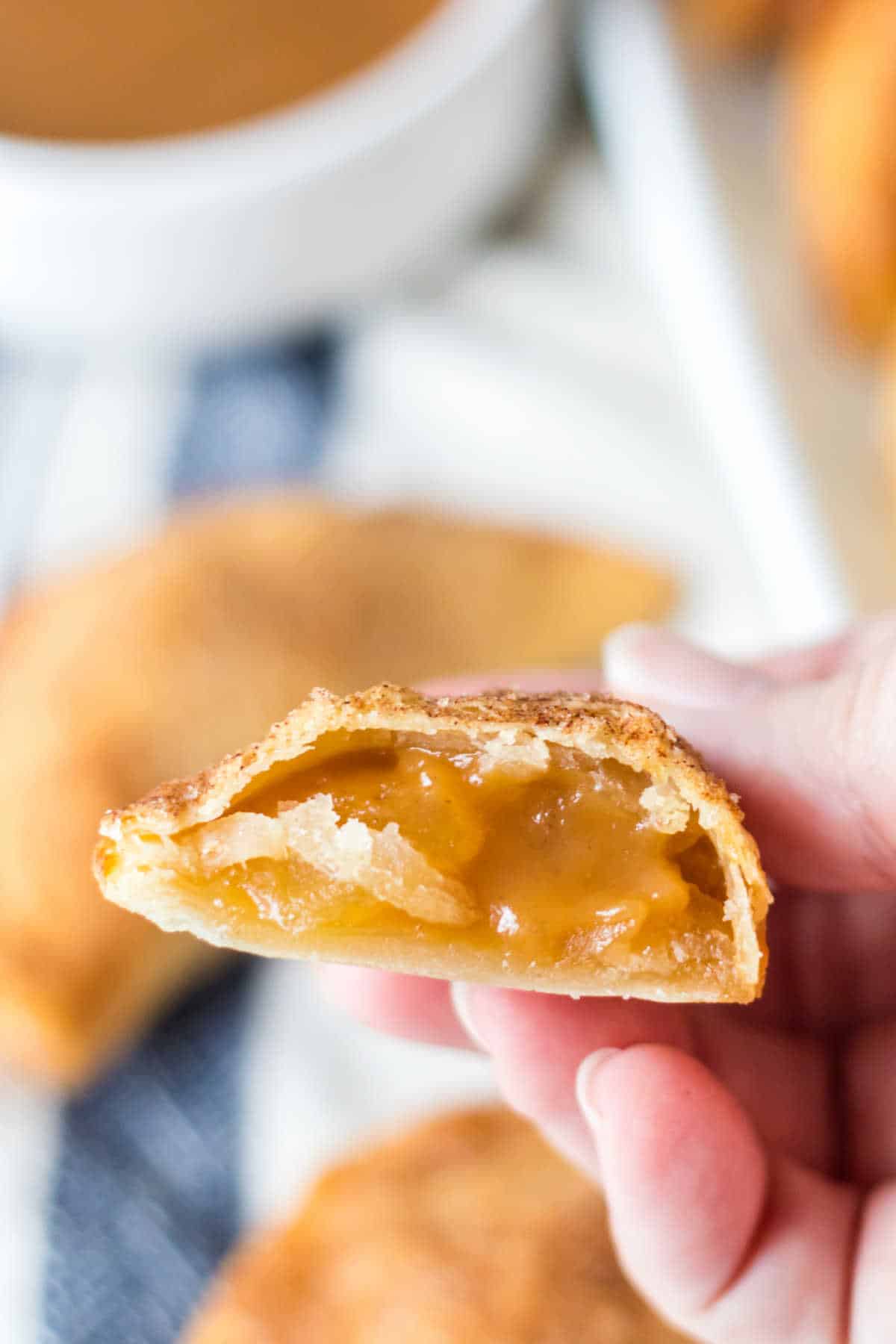 A hand holding a caramel apple empanada cut in half.