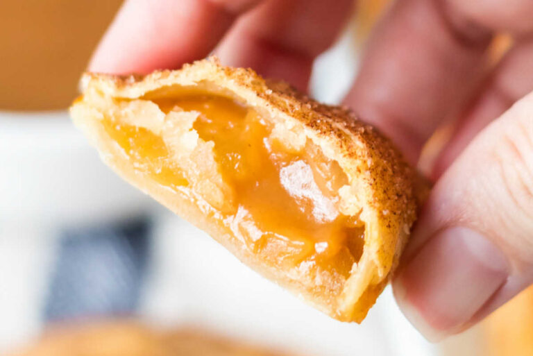 A hand holding a caramel empanada cut in half.