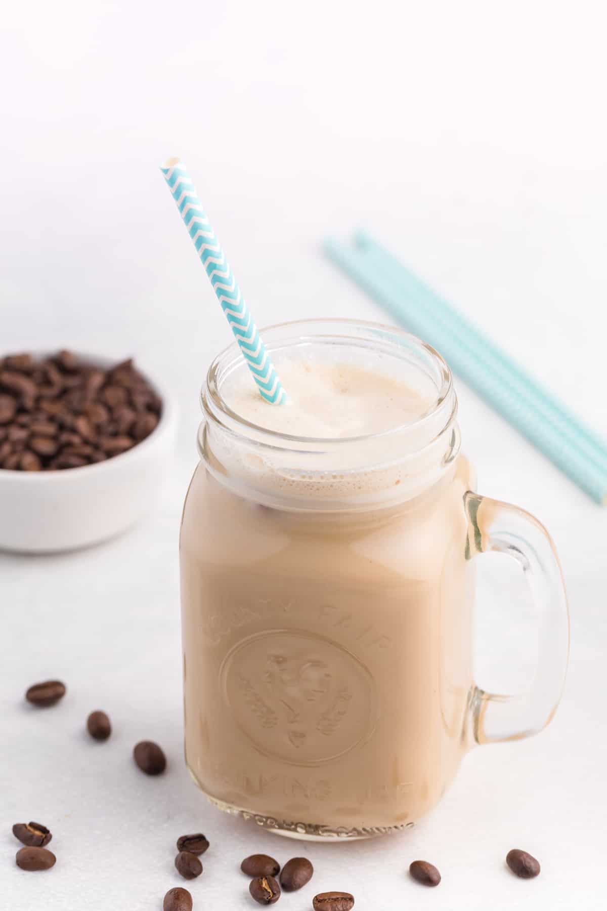 A glass jar with iced coffee and a straw.