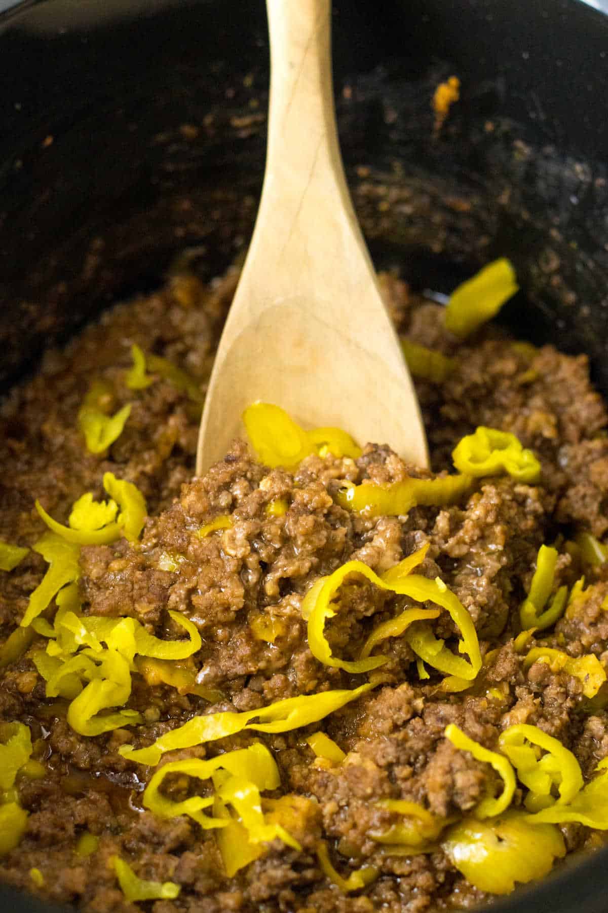 A slow cooker with Mississippi beef and a wooden spoon.