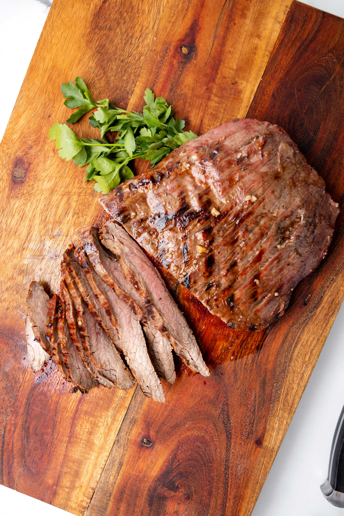 Grilled flank steak on a wooden cutting board with slices cut.