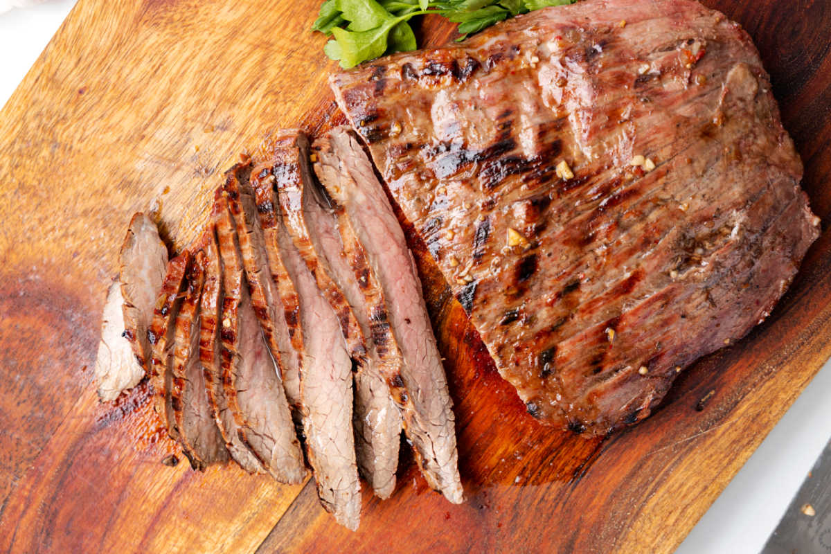 Grilled flank steak on a wooden cutting board with pieces sliced.