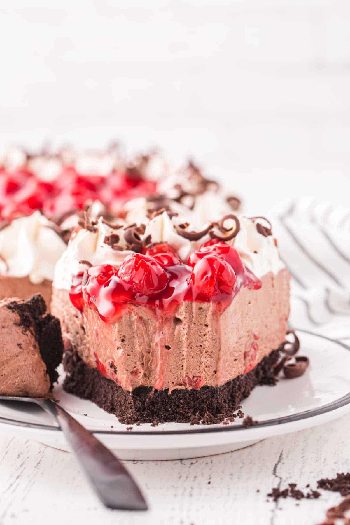A slice of black forest cheesecake on a plate with a bite off the end.
