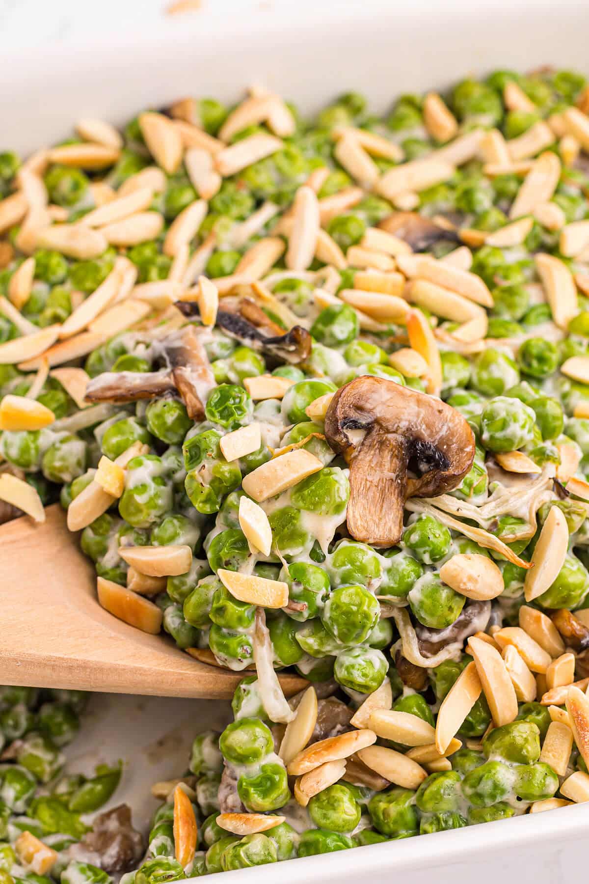 Company peas in a casserole dish with a wooden serving spoon.