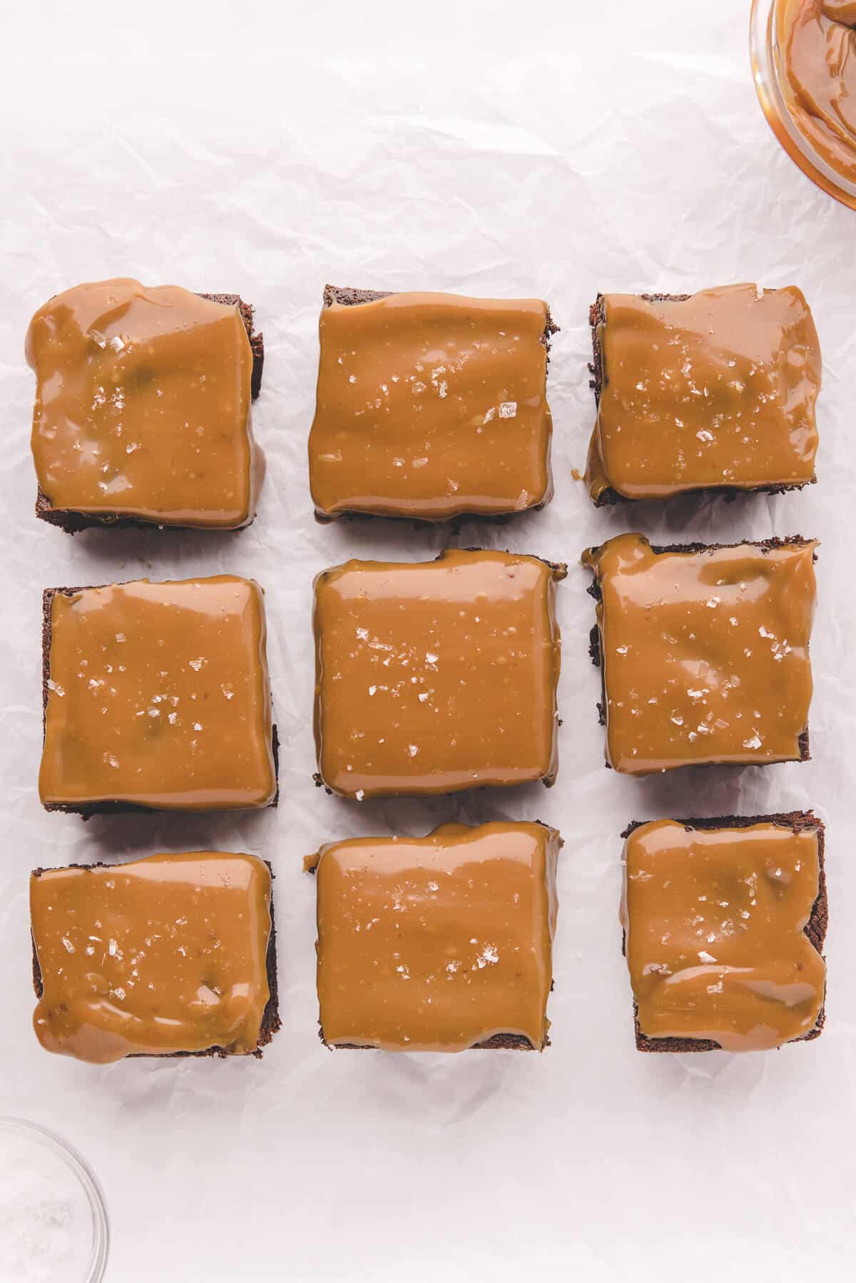 Salted caramel brownies cut into squares on piece of parchment paper.