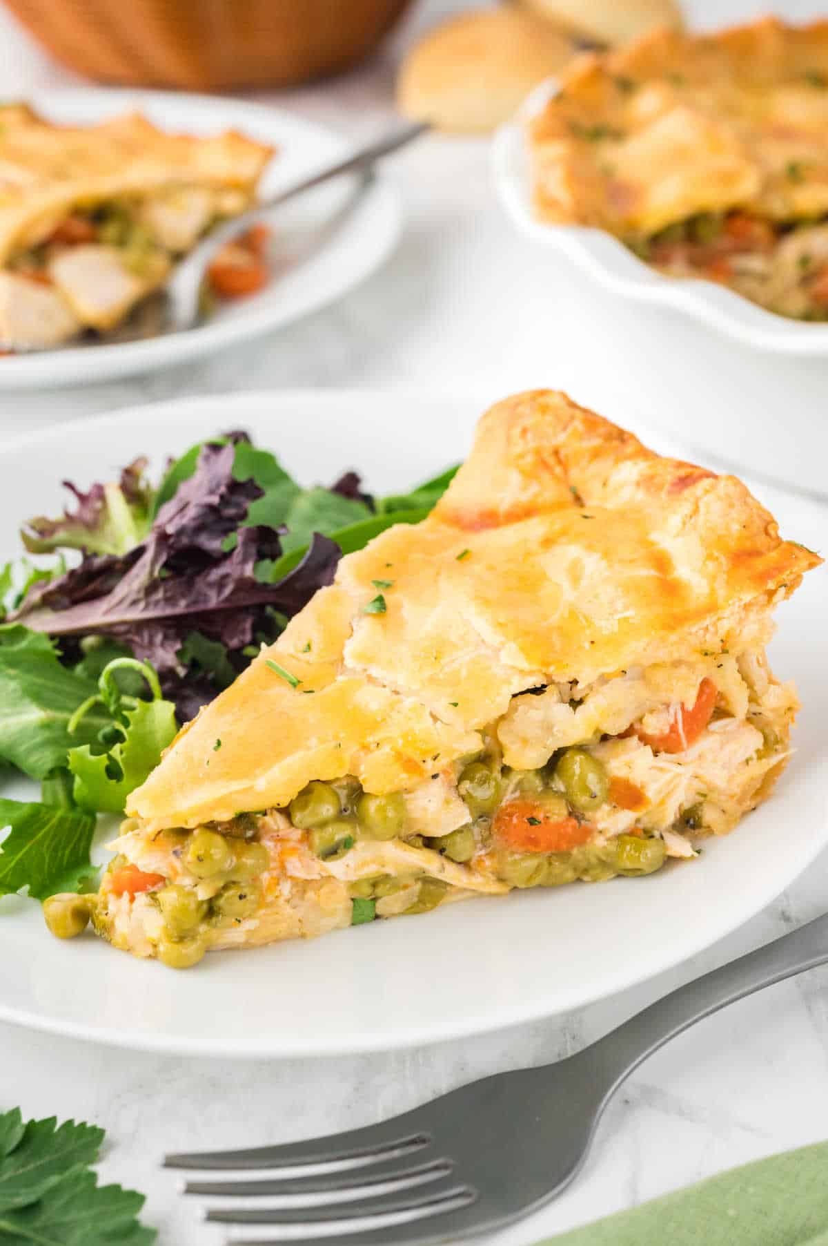 A slice of chicken pot pie on a plate with salad.