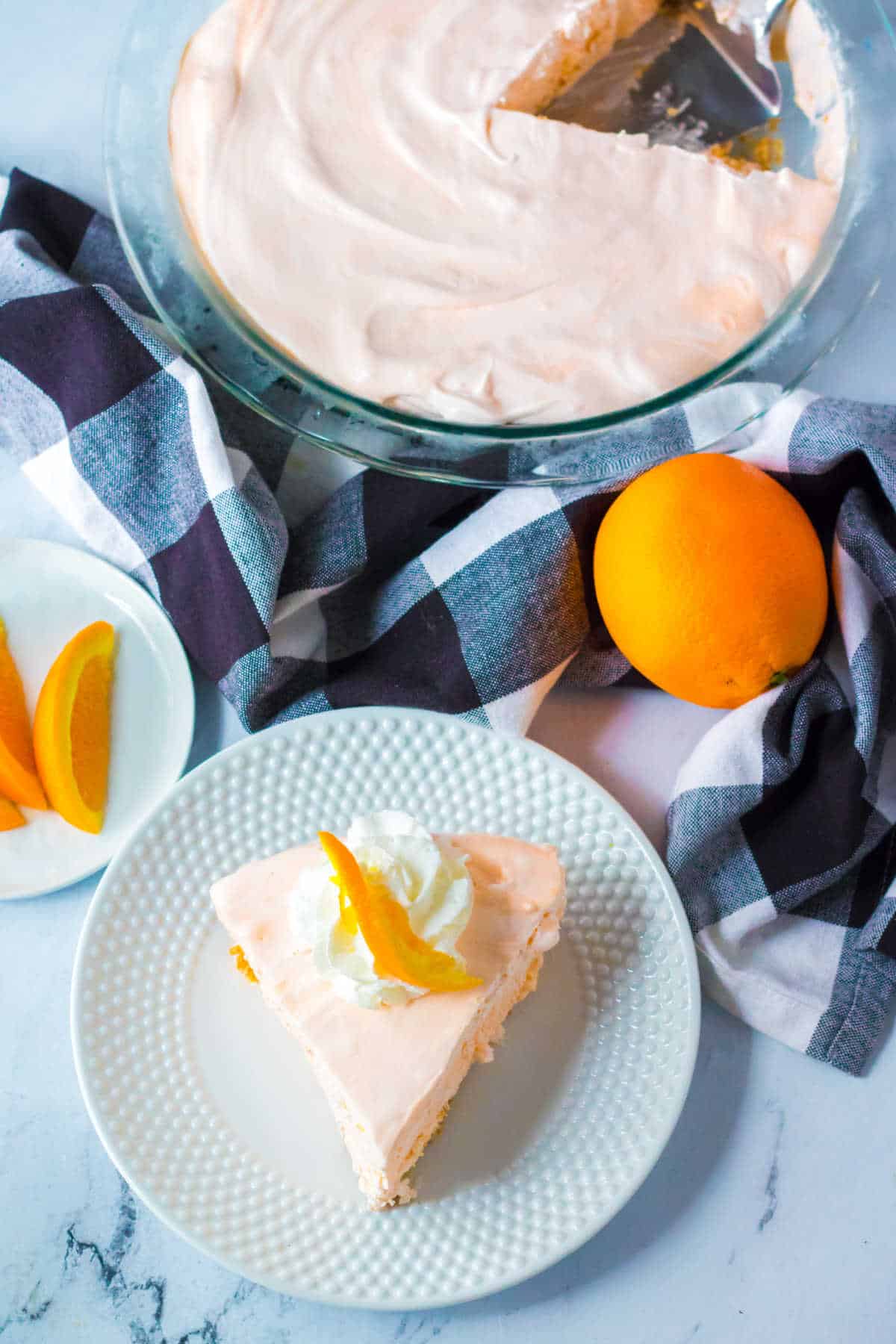 A slice of orange creamsicle pie on a plate with the pie plate showing the slice cut out.