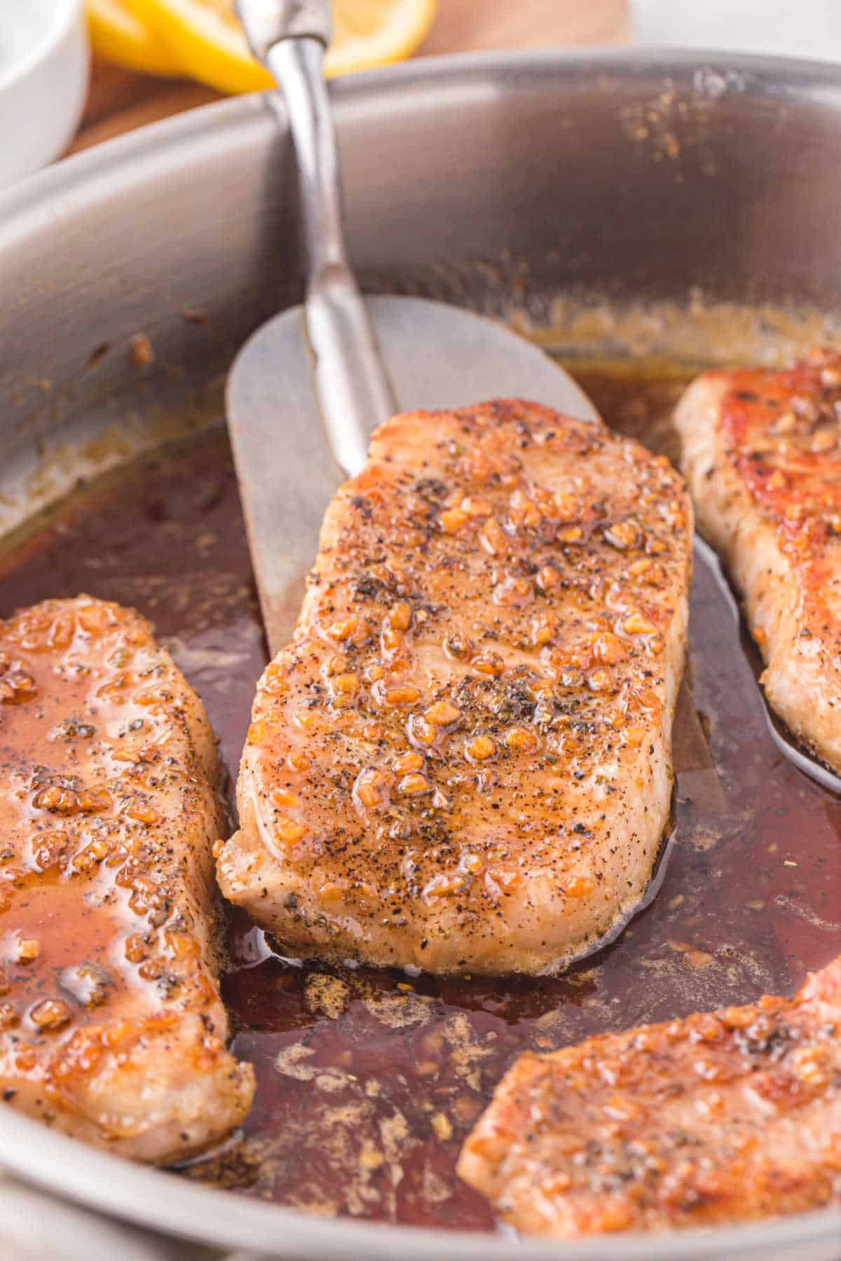 Honey garlic pork chops in a pan with a serving spatula.