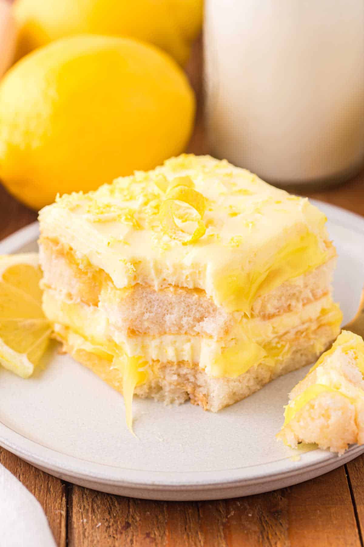 A piece of lemon tiramisu on a plate with a bite out of it.