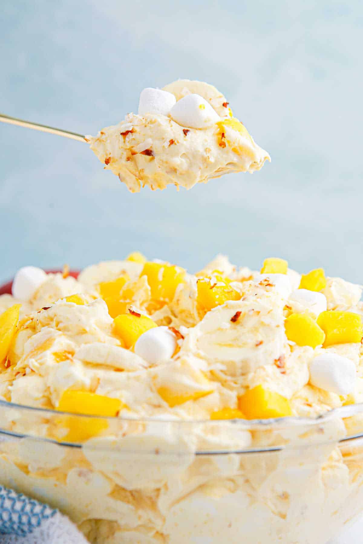 A spoon with mango banana marshmallow salad over a bowl of the salad.