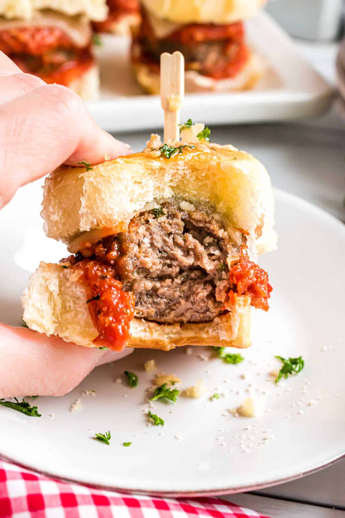 A hand holding a meatball slider with a bite out of it.