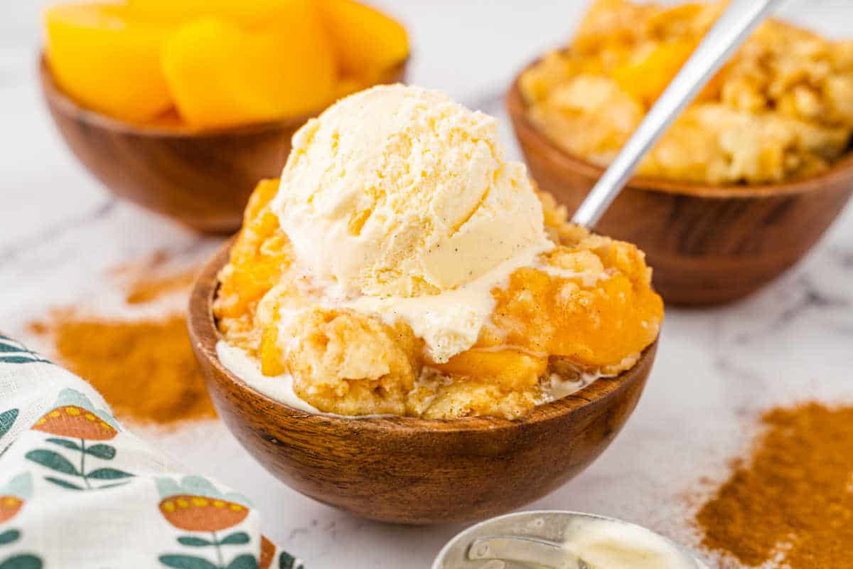 Peach cobbler dump cake in a bowl with a spoon topped with vanilla ice cream.