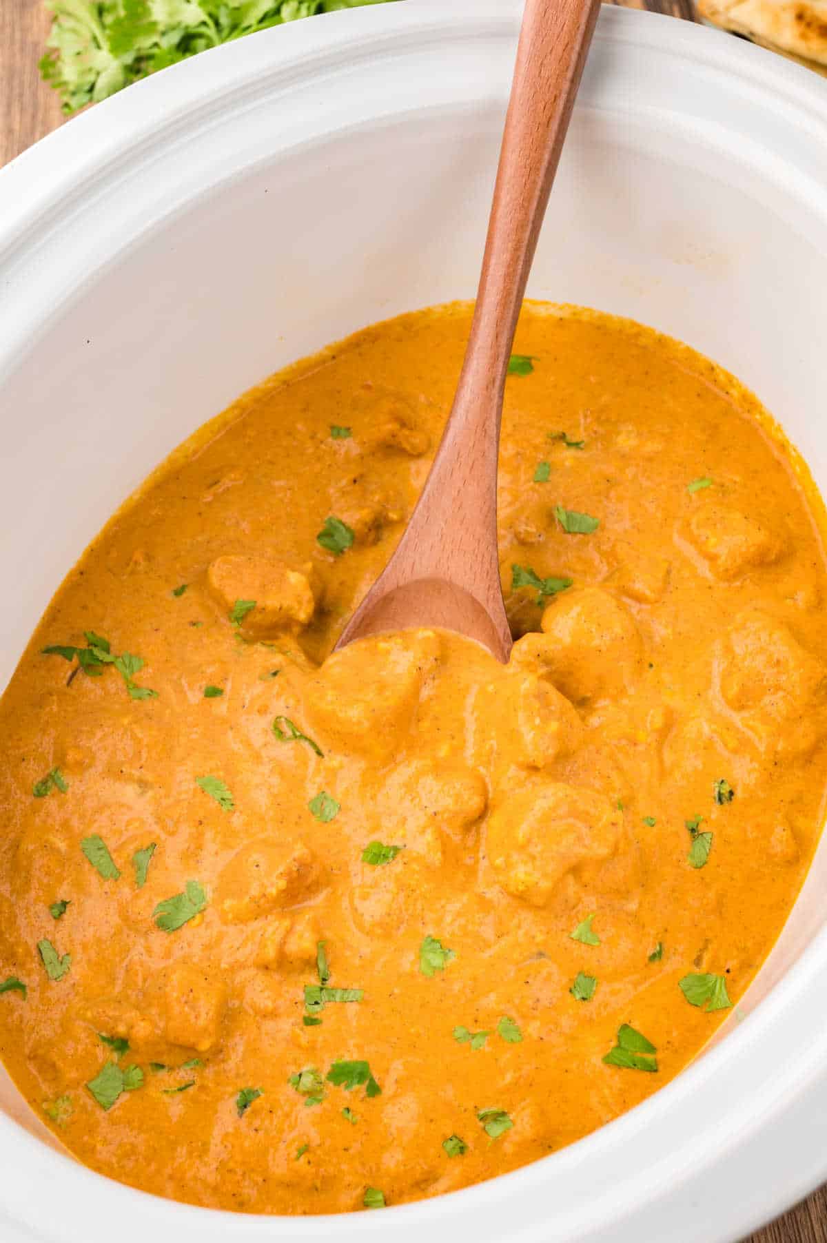 Butter chicken in a slow cooker with a wooden spoon.