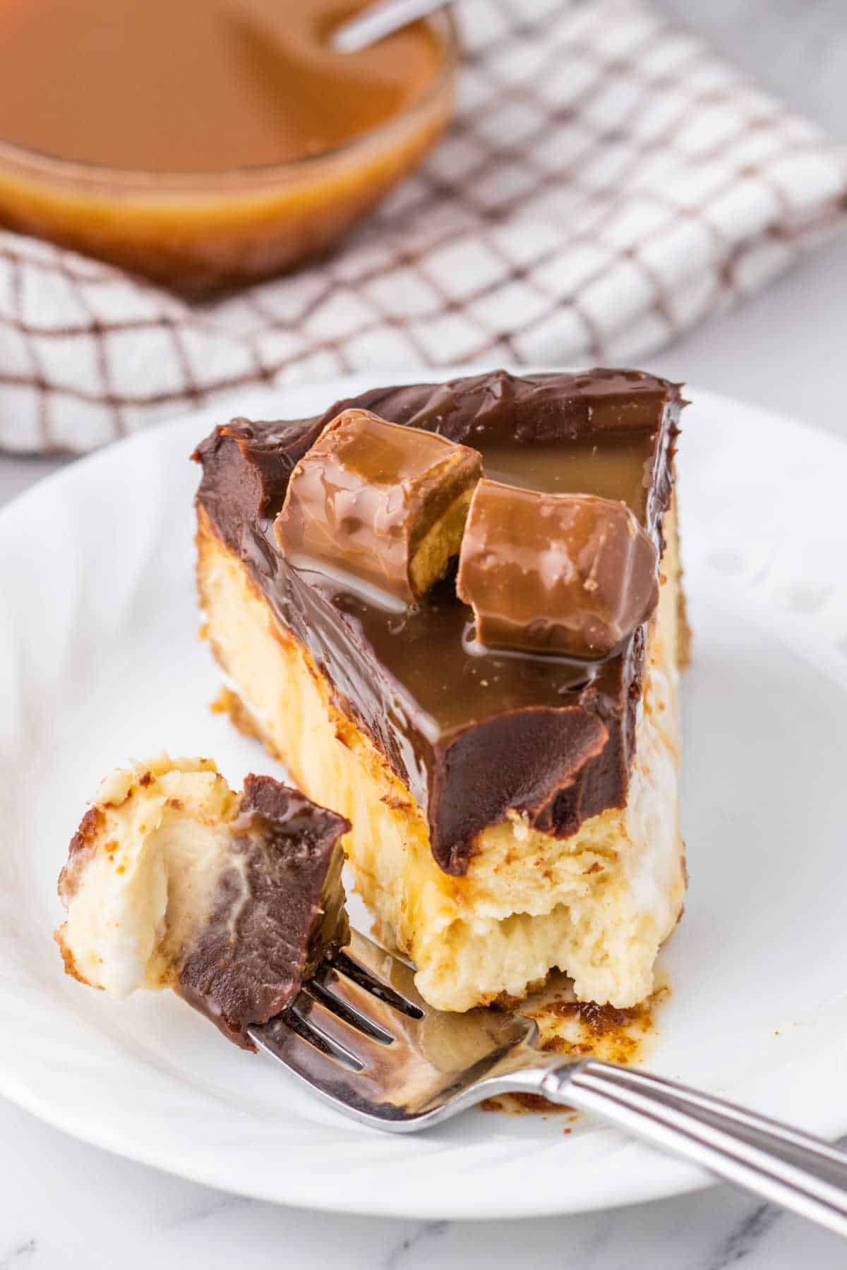 A slice of Twix Cheesecake with a fork and a bite off the end.