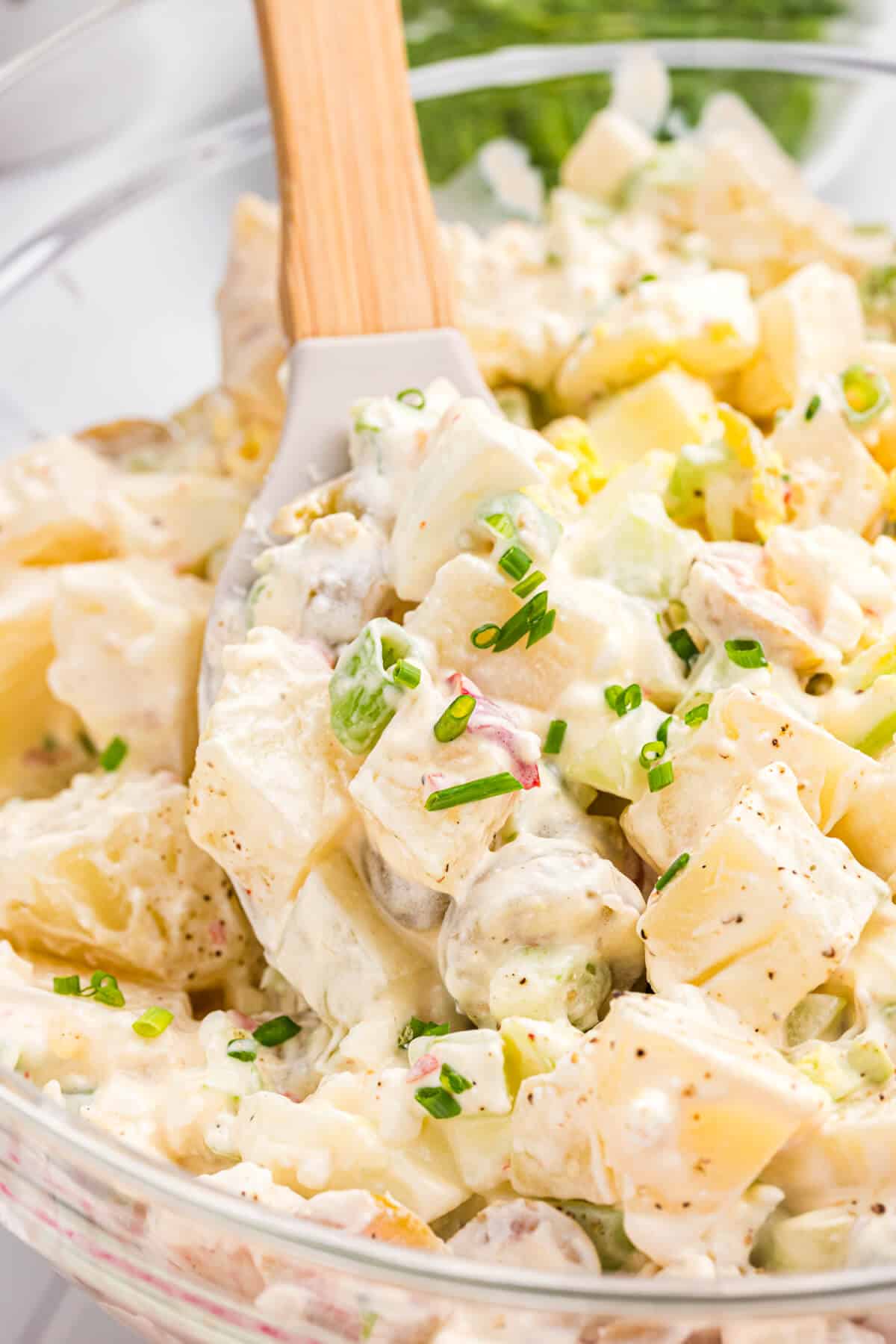 A bowl of cheese potato salad with a wooden spoon.