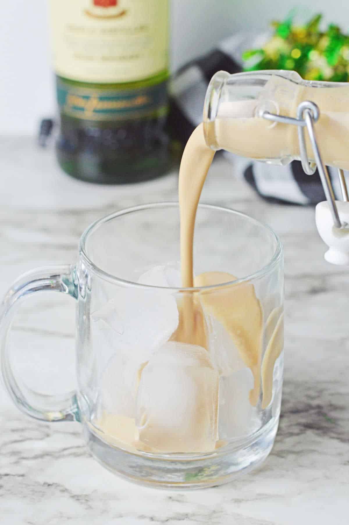 A glass bottle pouring homemade Irish cream into a glass with ice.
