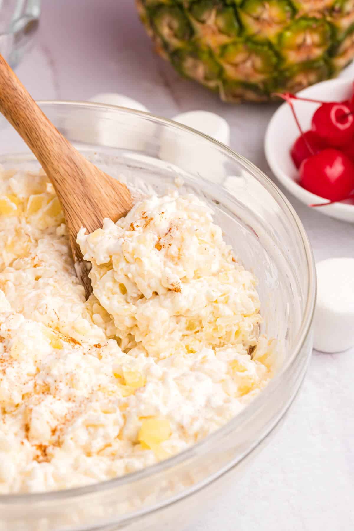 A bowl of pineapple rice pudding with a wooden spoon in it.