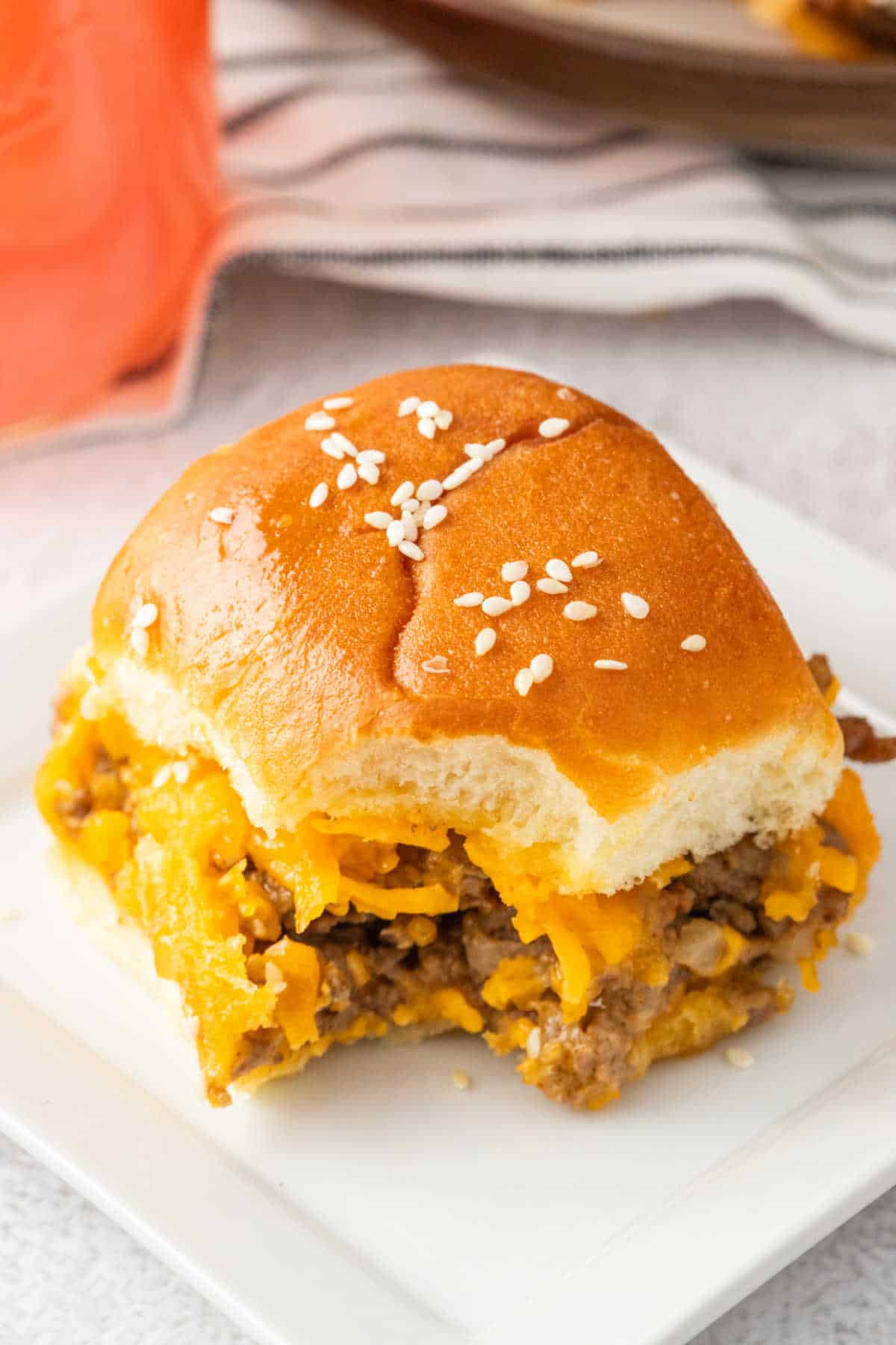 A cheeseburger slider with a bite out of it on a plate.