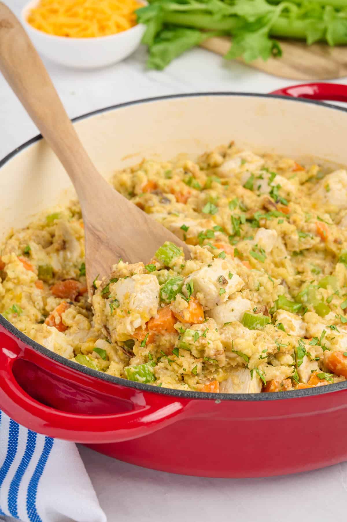 A pot of chicken and stuffing with a wooden spoon in it.