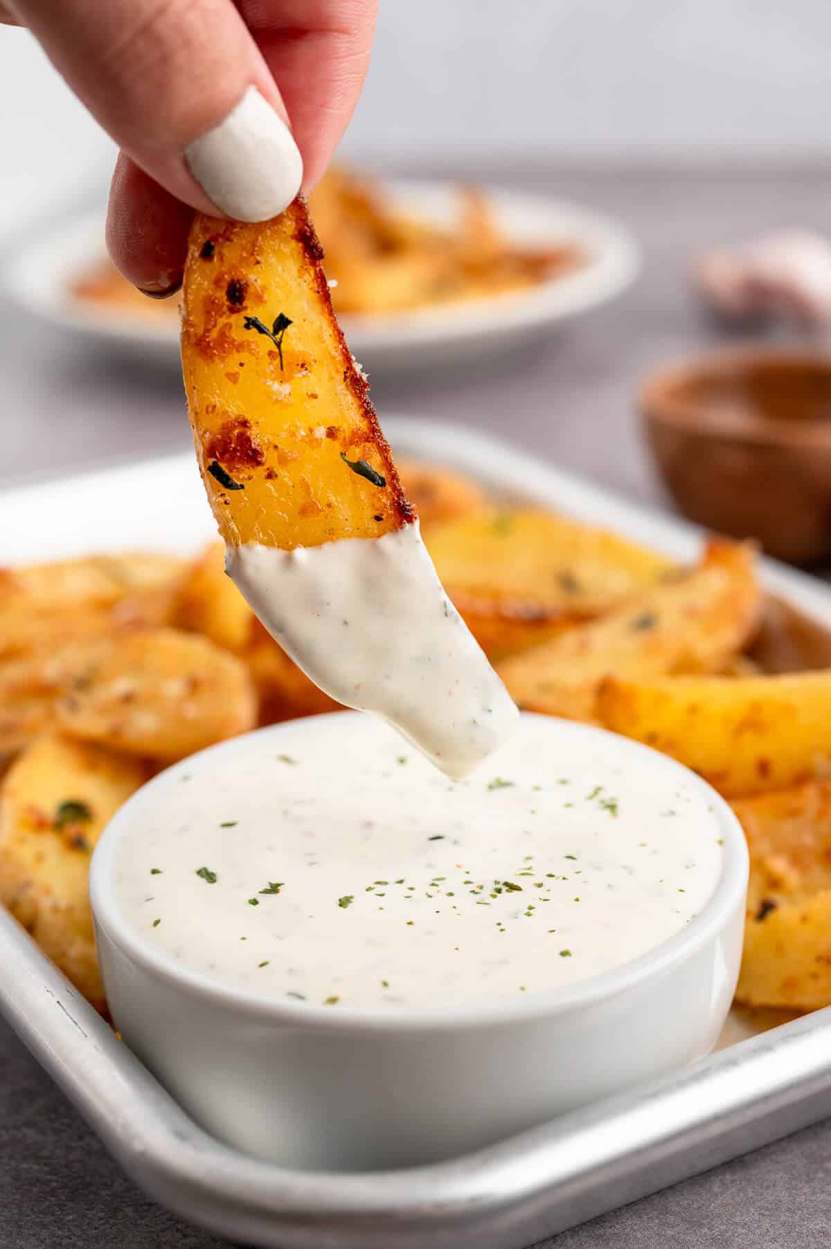 A hand dipping parmesan thyme roasted potato into ranch dip.