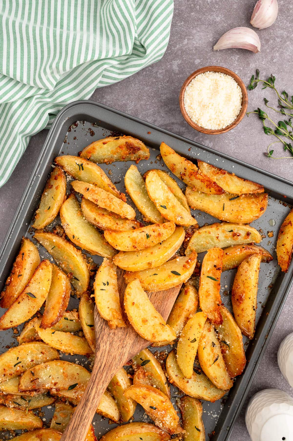 Parmesan thyme roasted potatoes on a baking sheet with a wooden spatula.