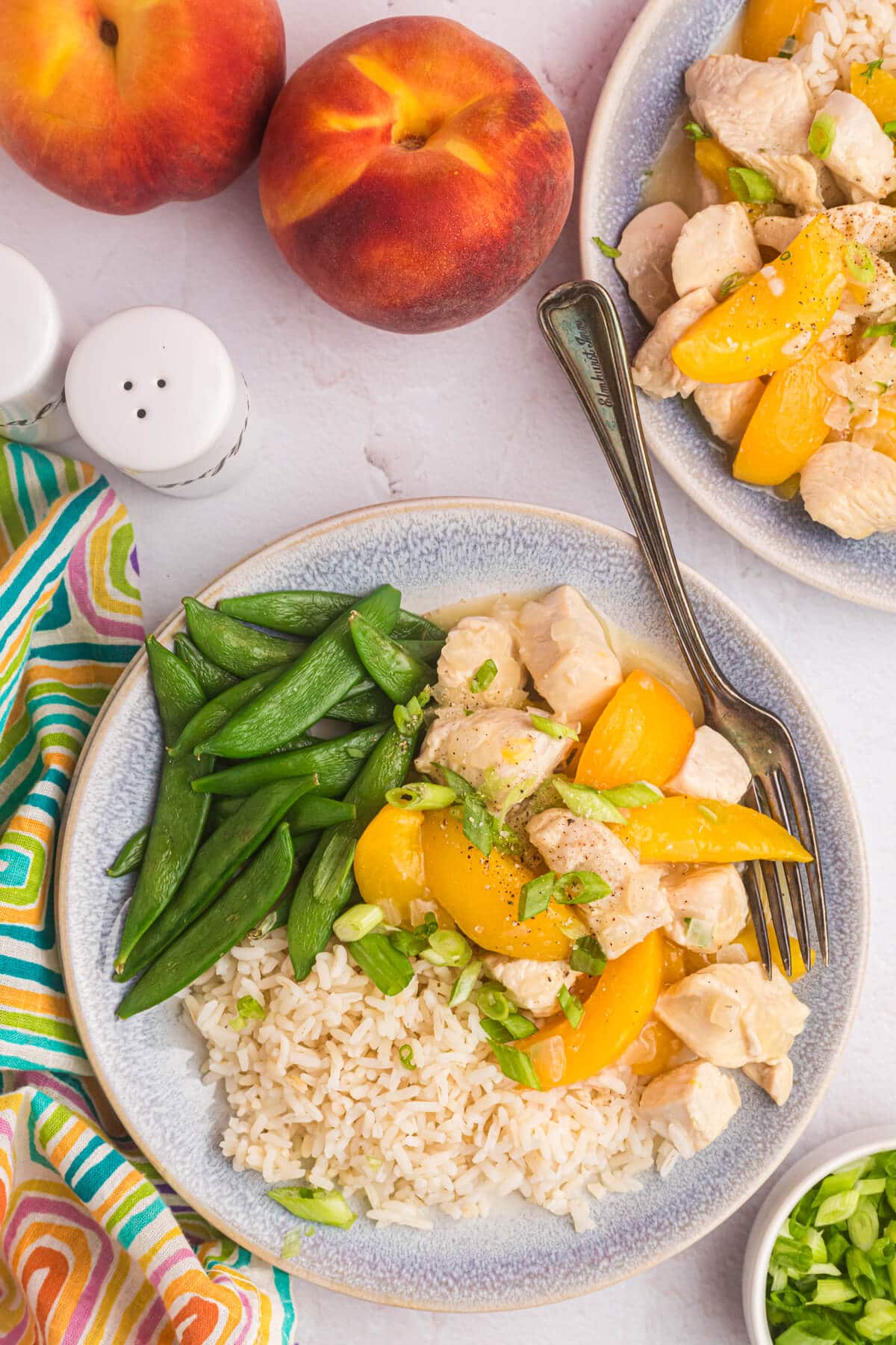 Peach chicken on a plate with snow peas and rice.