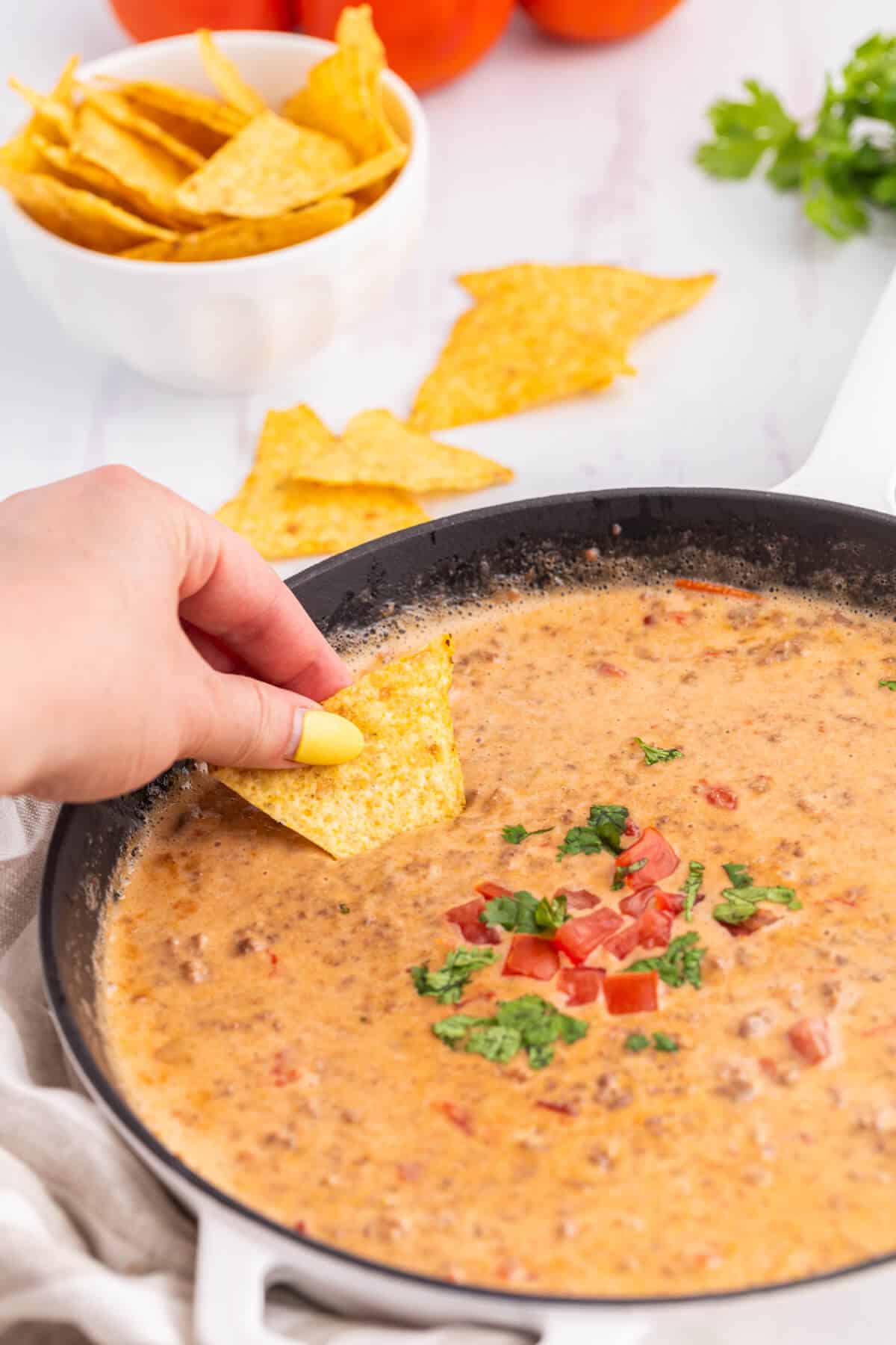 A hand dipping a tortilla chip in a skillet of Rotel dip.