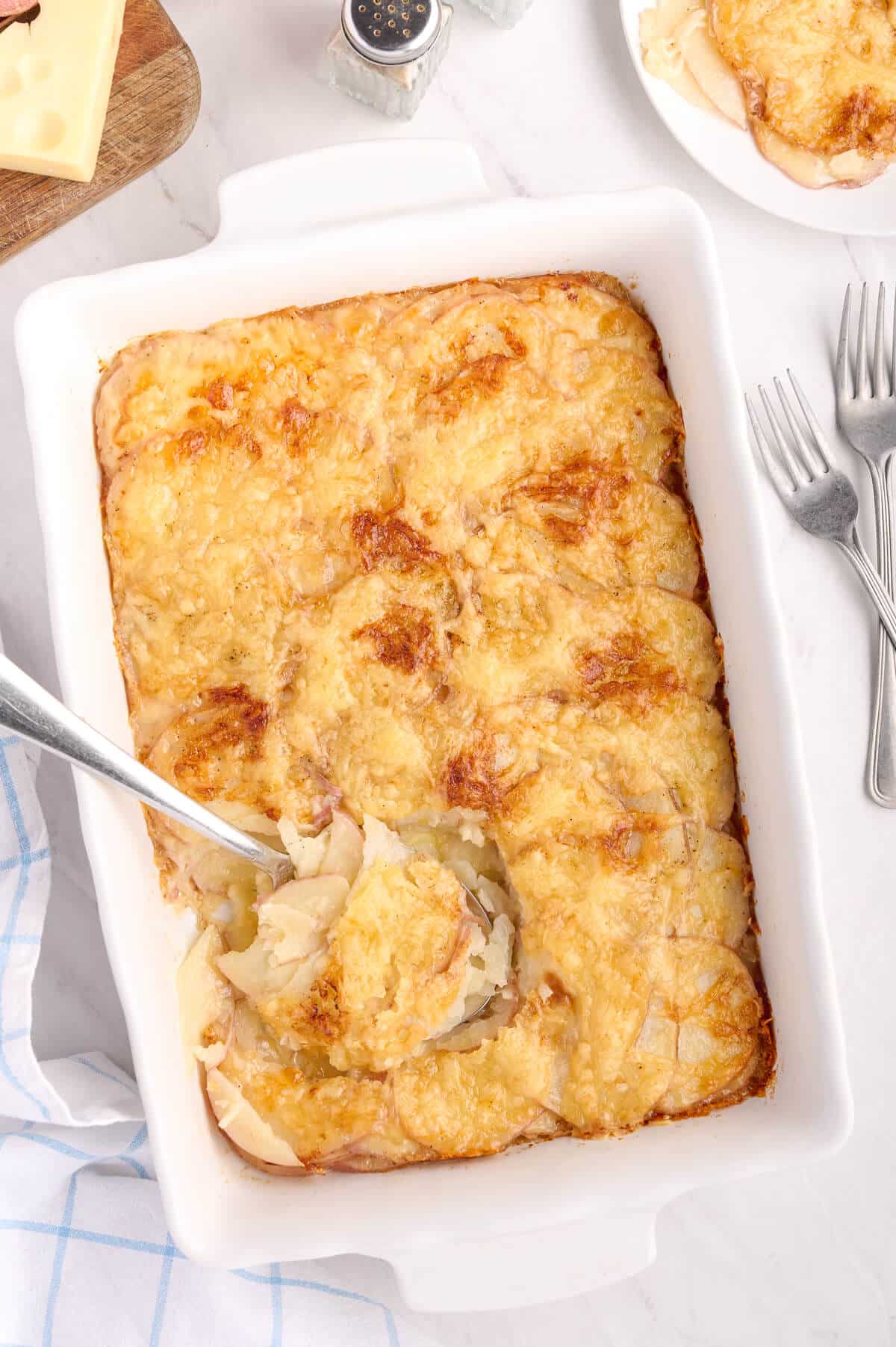 A baking pan of Swiss Potatoes with a serving spoon.