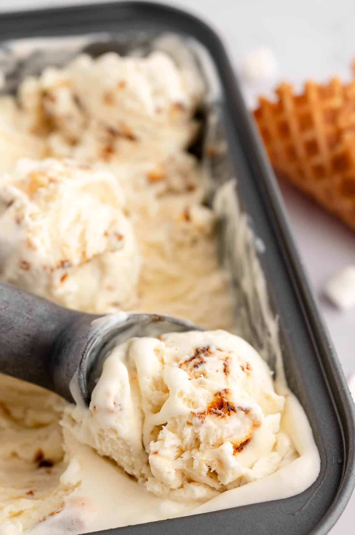 A loaf pan of toasted marshmallow ice cream with an ice cream scoop.