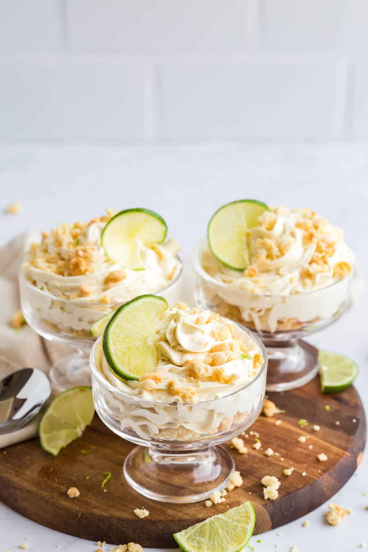 Three lime cheesecake parfaits on a wooden board.