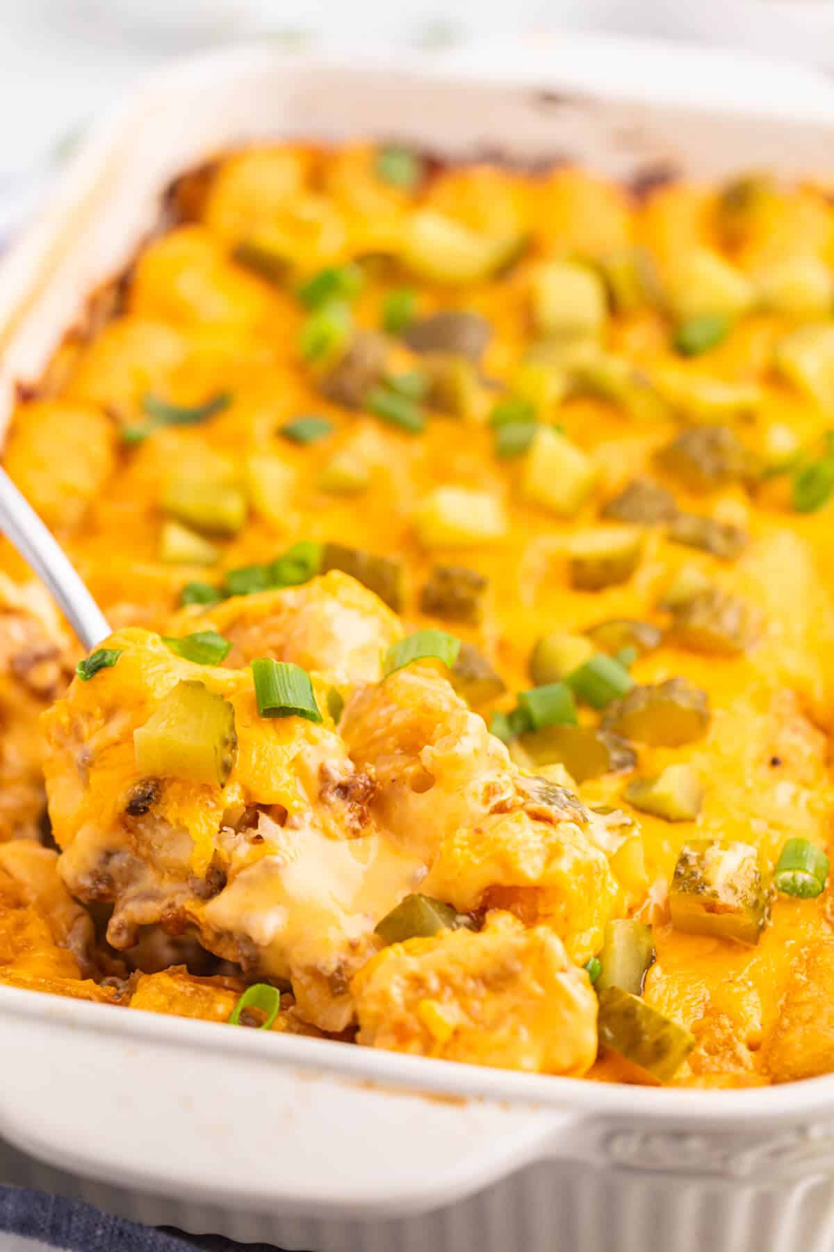 A serving spoon in a pan of cheeseburger tater tot casserole.