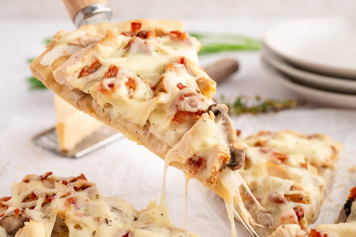 A slice of chicken bacon alfredo pizza on a spatula.