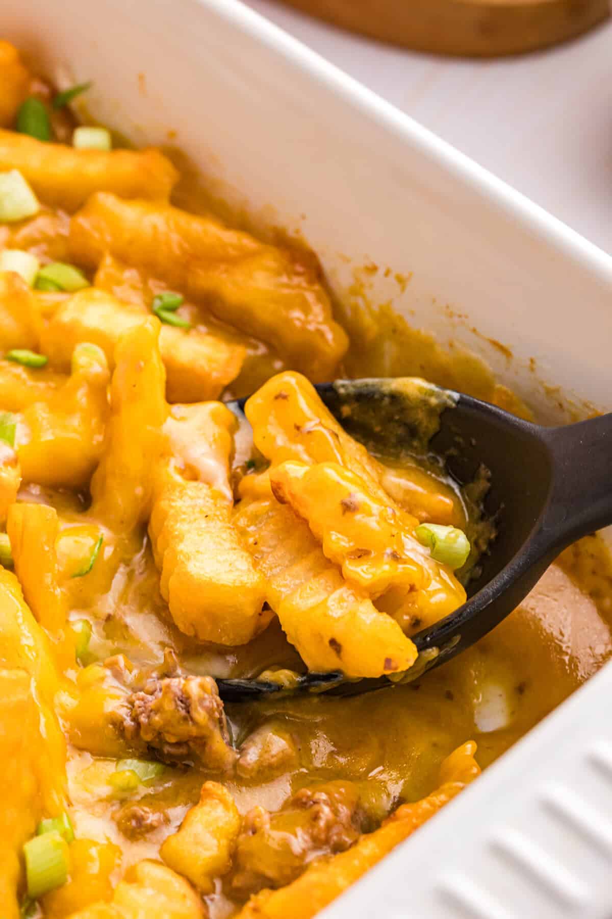 French fry casserole with a serving spoon in the pan.