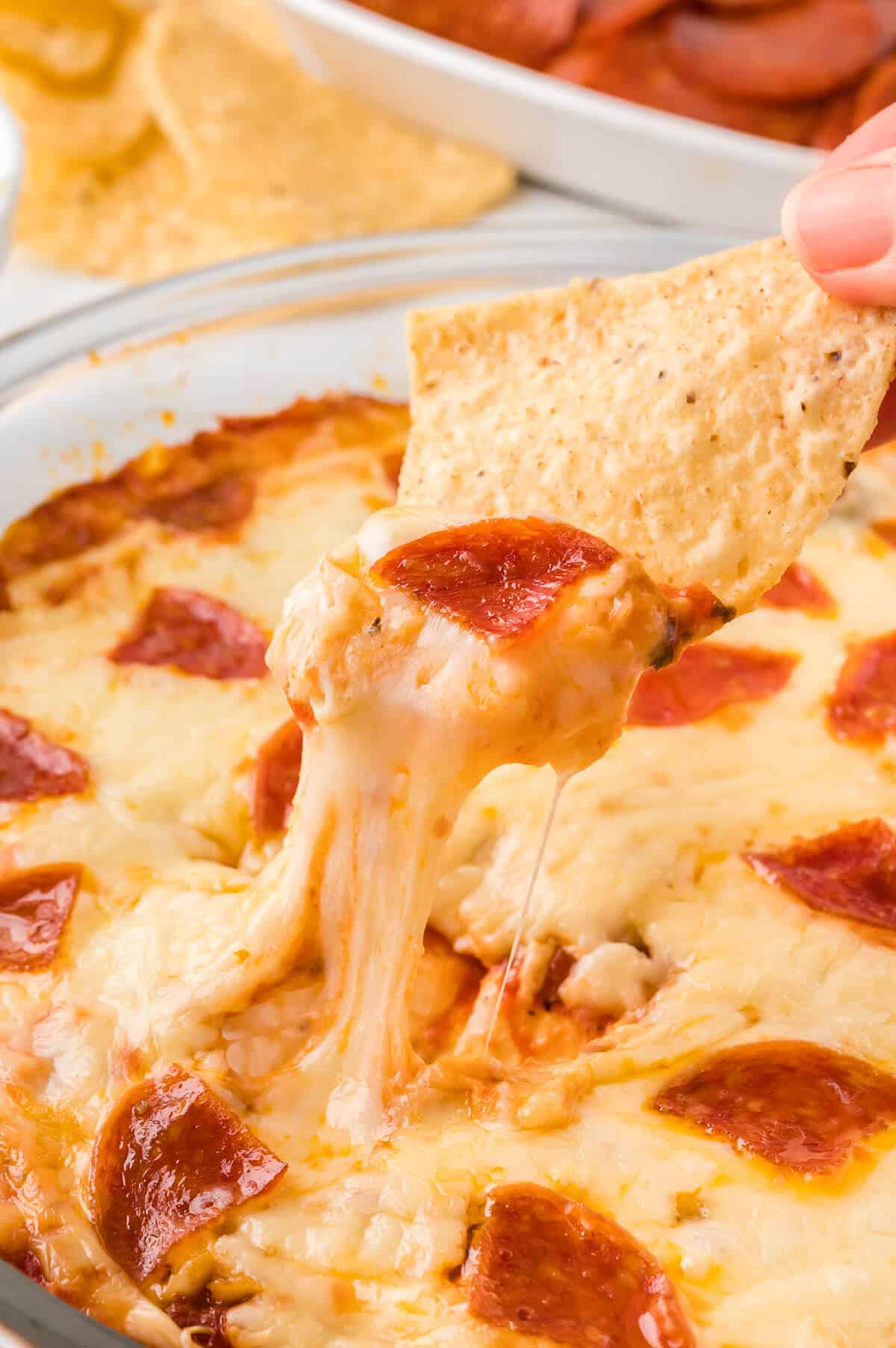 A hand dipping a tortilla chip in pizza dip.