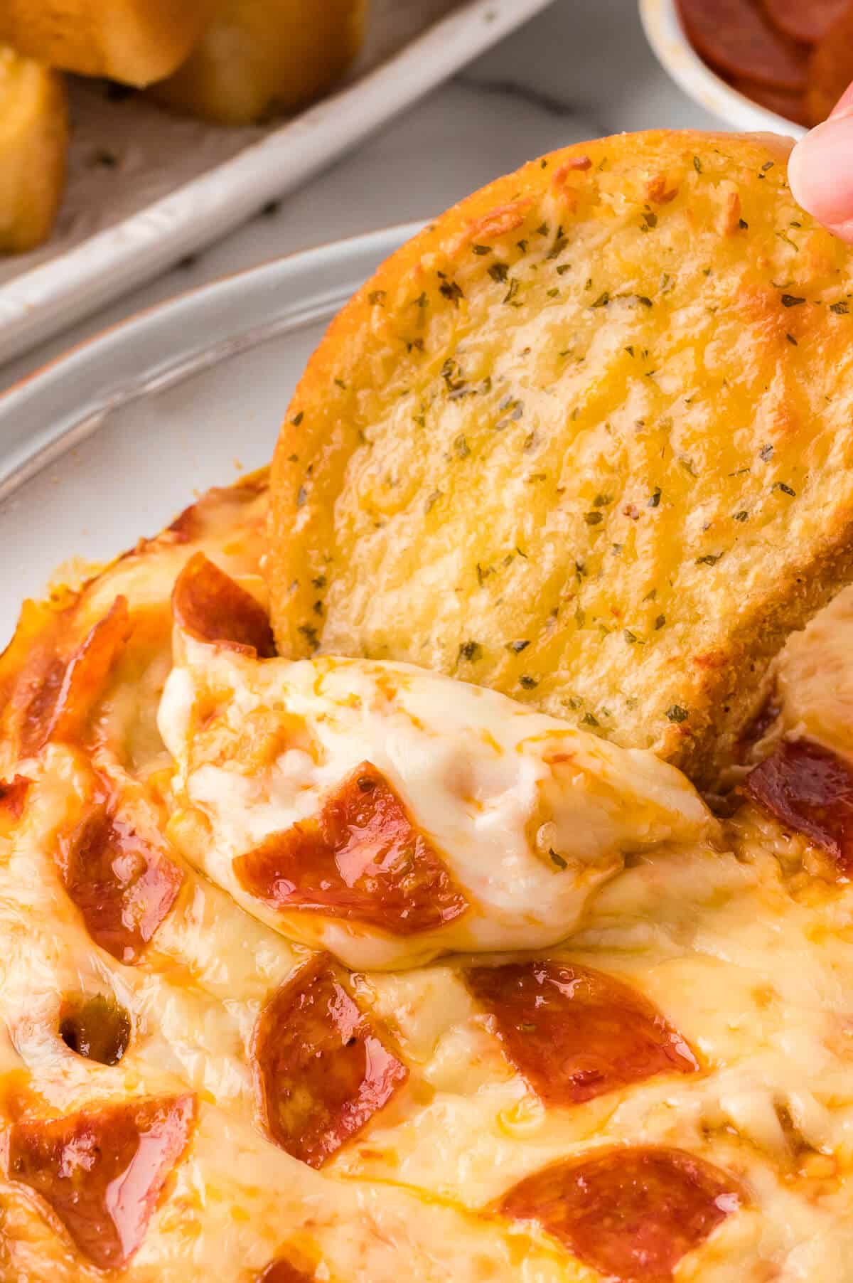 A hand dipping garlic bread in pizza dip.