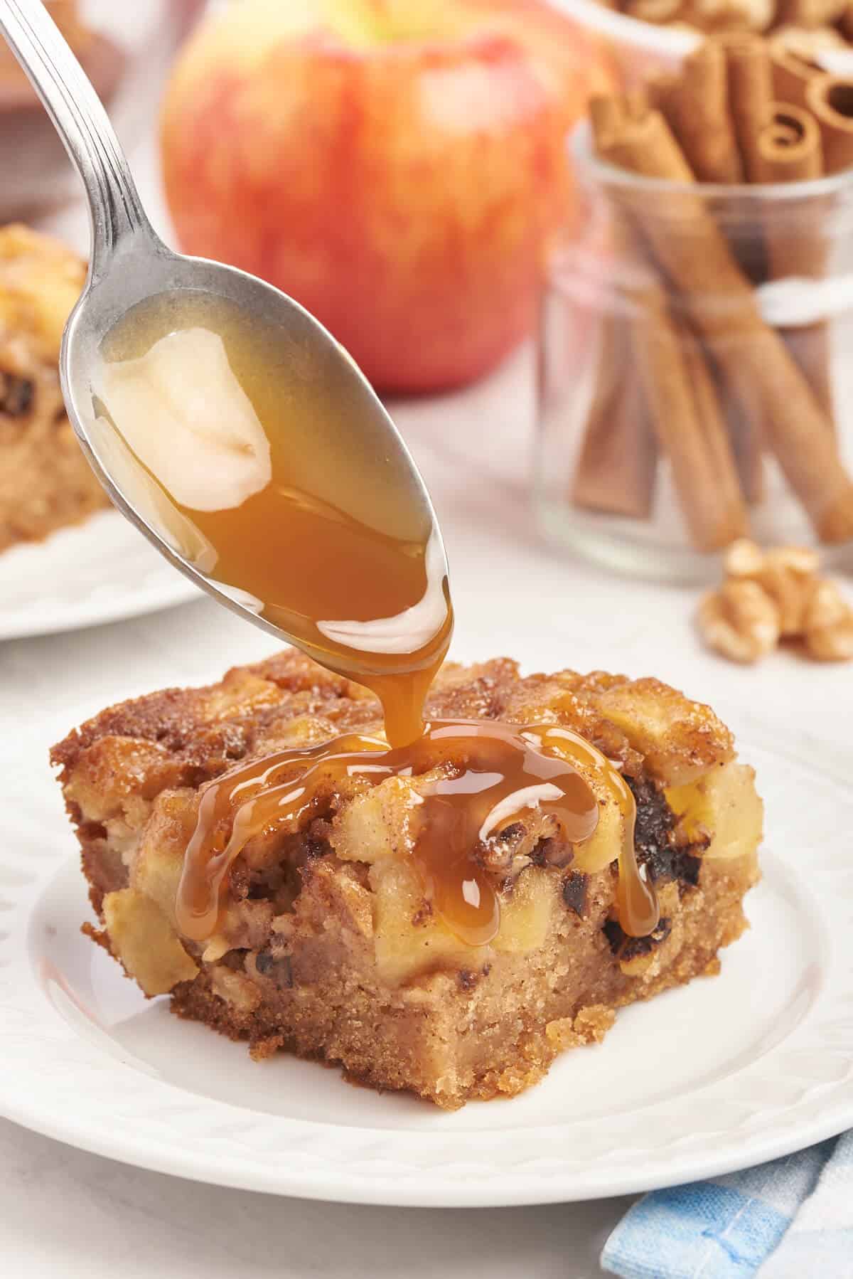 A spoon drizzling caramel over a slice of Nobby apple cake.