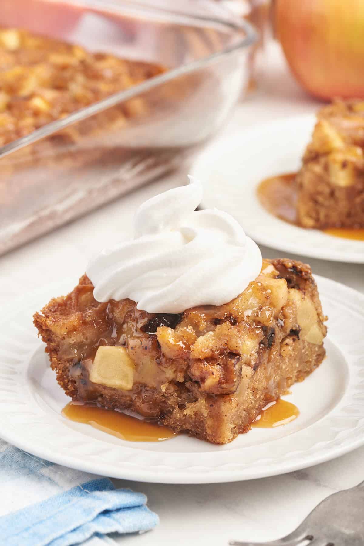 A piece of nobby apple cake on a plate topped with whipped cream.