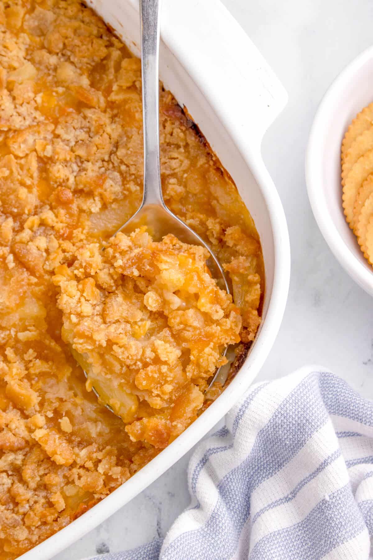 Pineapple casserole in a pan with a serving spoon.