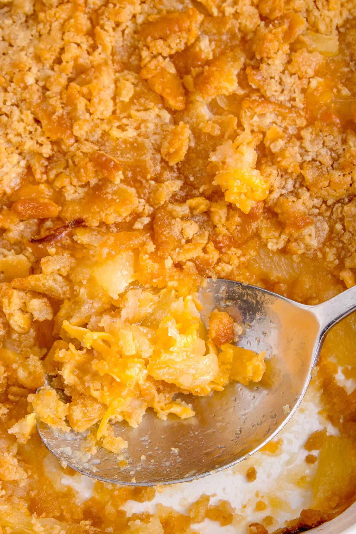 A serving spoon in a pan of pineapple casserole.