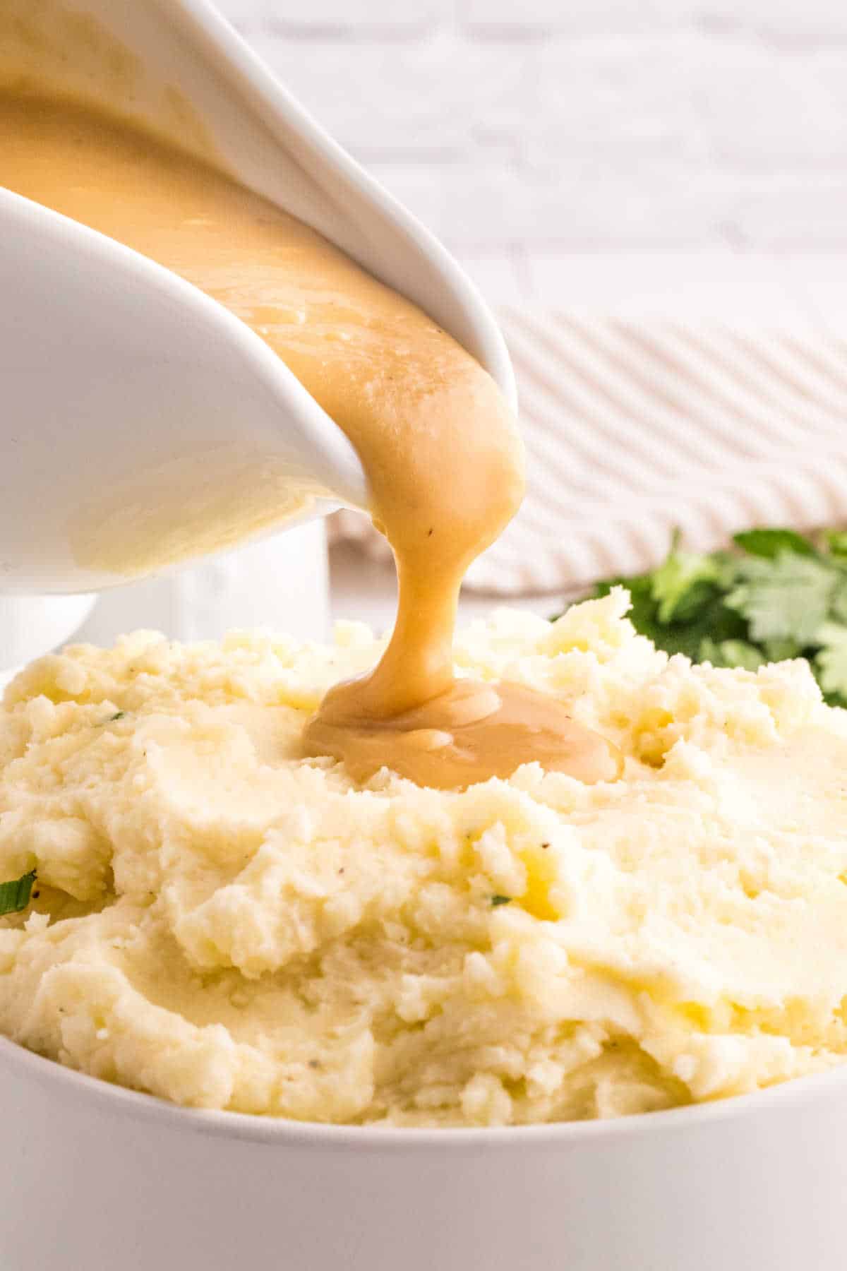 A gravy boat pouring brown gravy on mashed potatoes.