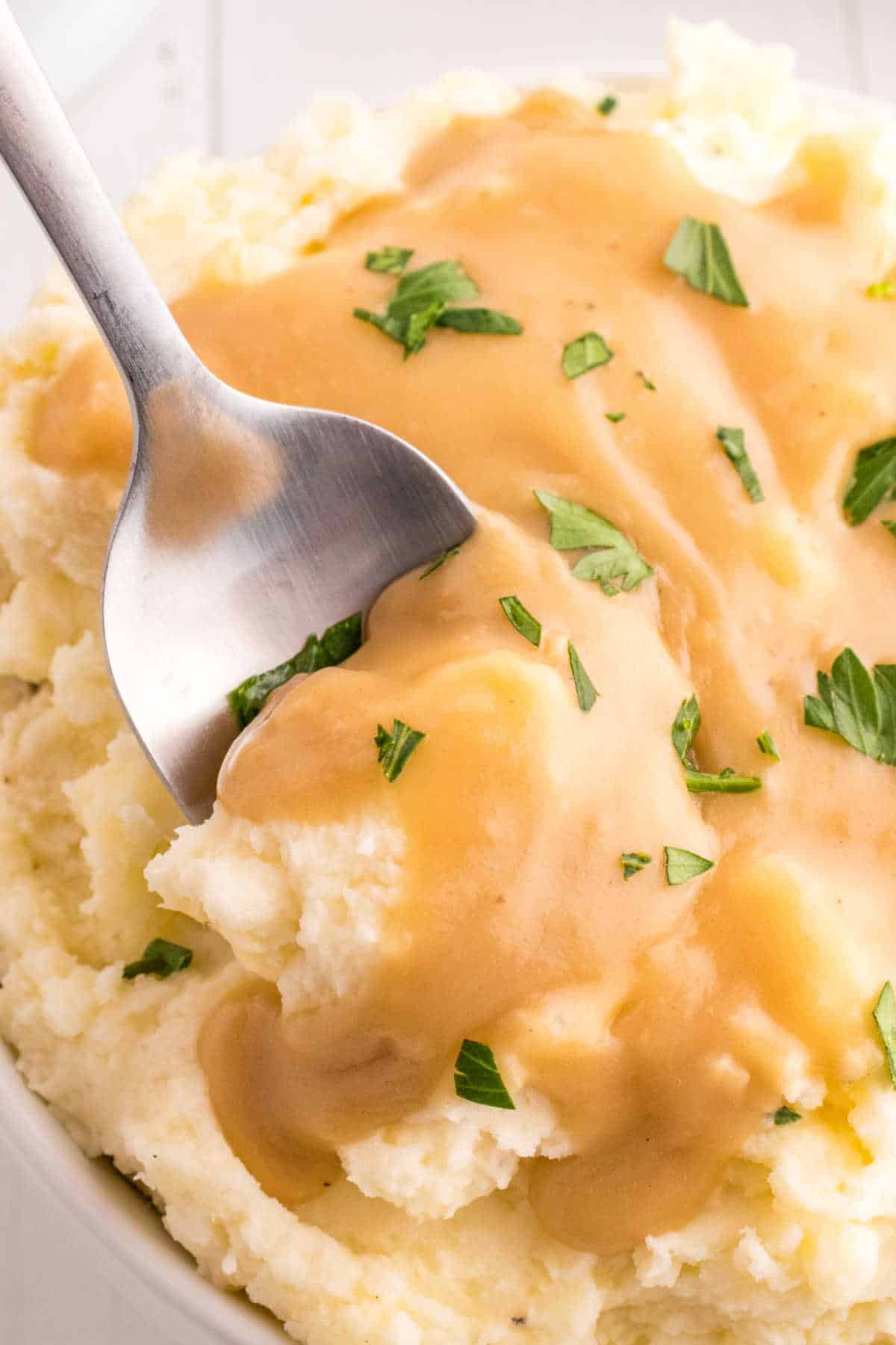 A serving spoon in a bowl of mashed potatoes topped with brown gravy.