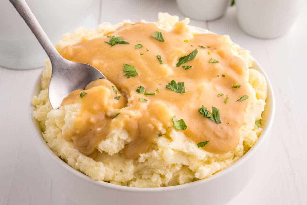 A bowl of mashed potatoes topped with brown gravy and a serving spoon in the bowl.