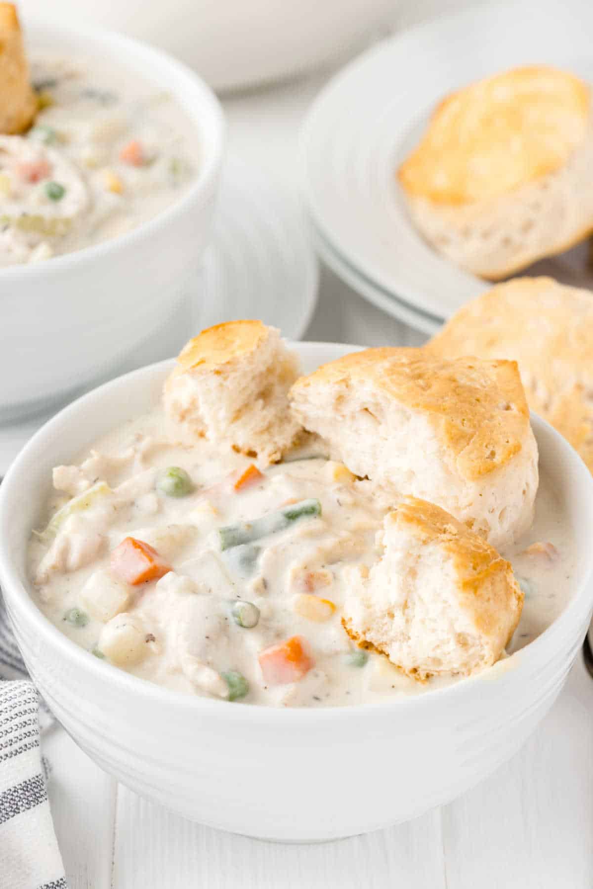 A bowl of chicken pot pie soup with buns.