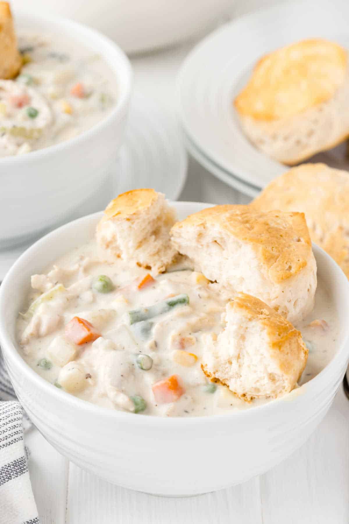 A bowl of chicken pot pie soup with buns.
