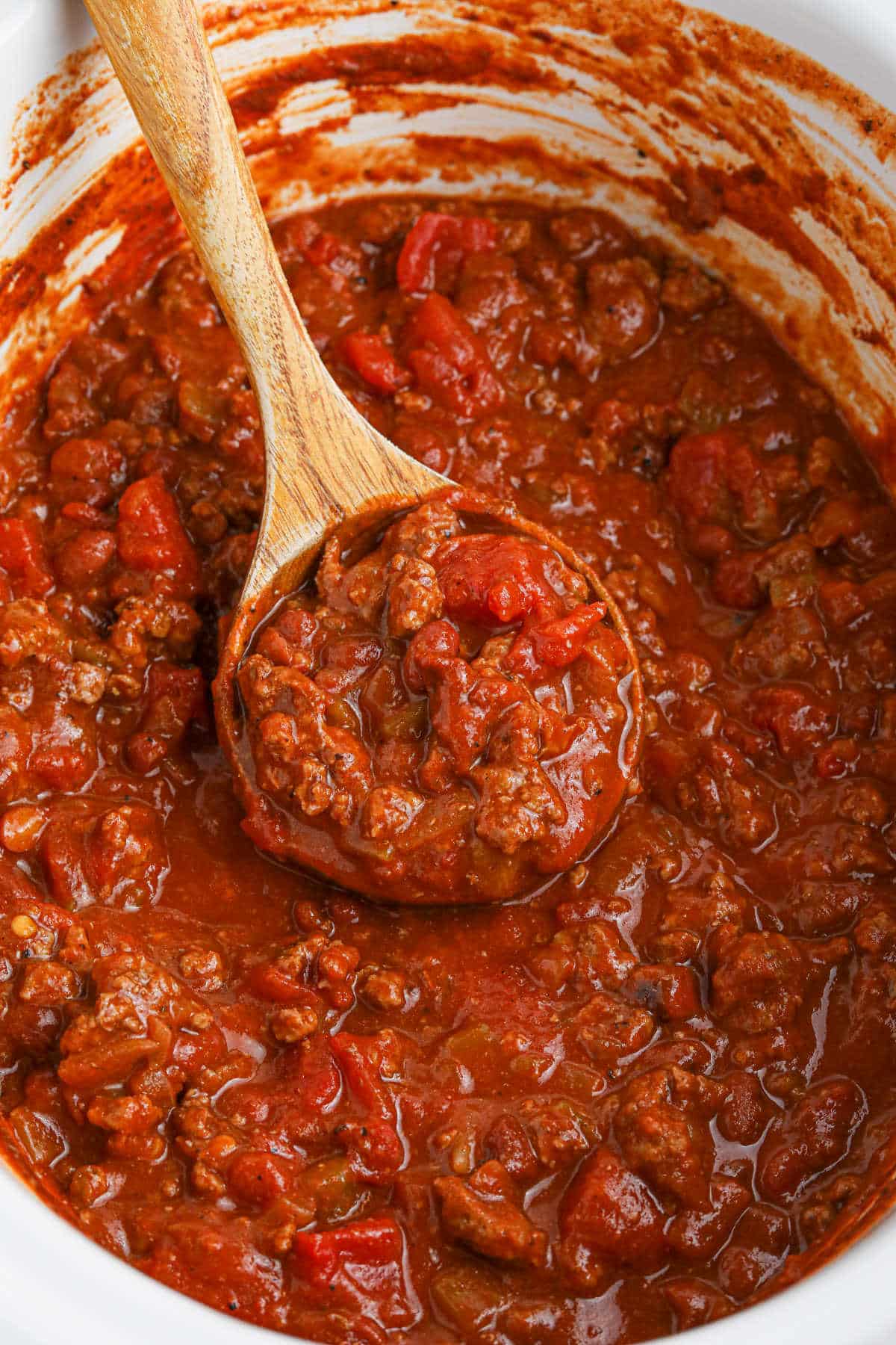 Frito chili pie in a crockpot with a wooden spoon.