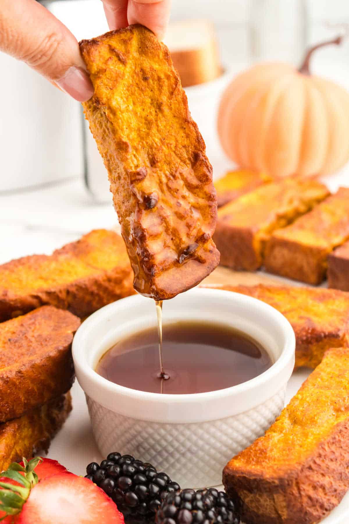 A hand dipping an air fryer pumpkin French toast stick in maple syrup.