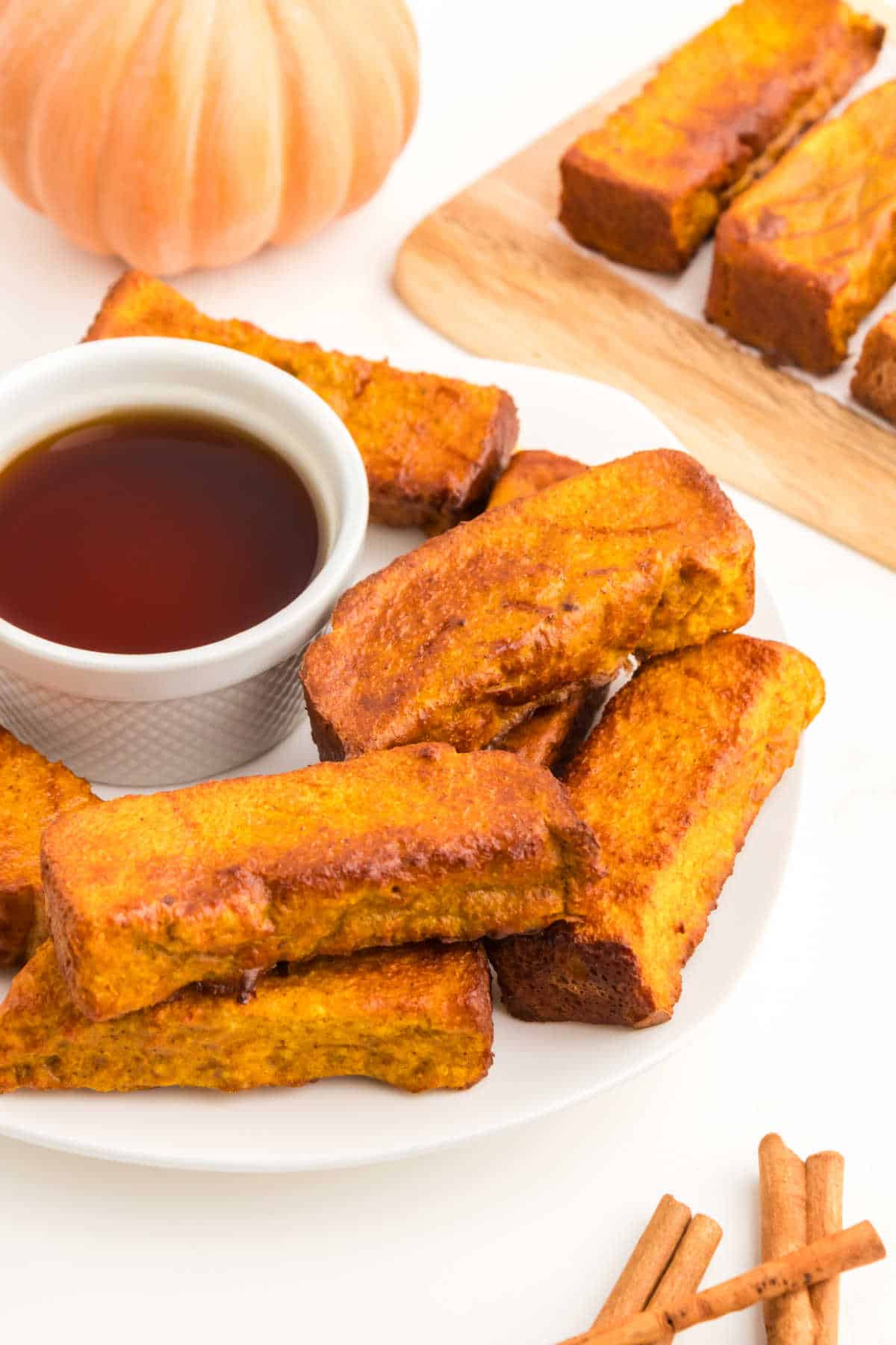 An air fryer pumpkin french toast sticks on a platter with maple syrup.