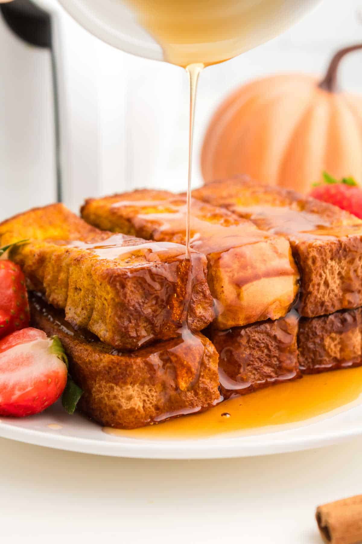 A pile of air fryer pumpkin french toast sticks with maple syrup drizzled on them.