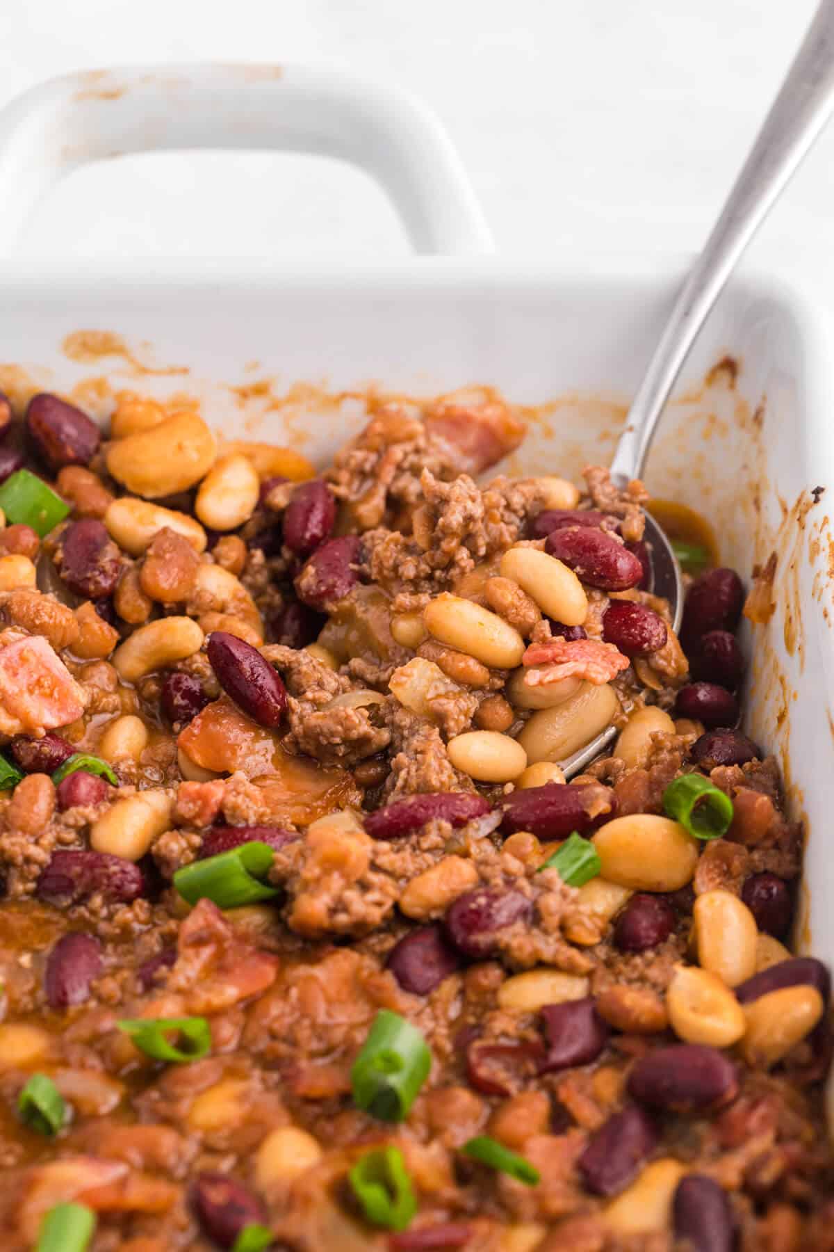 Baked bean casserole in a pan with a serving spoon.