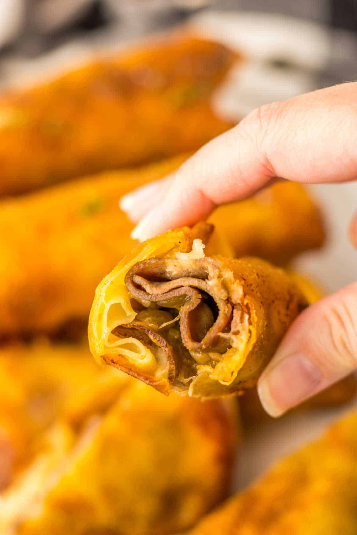 A hand holding a French dip egg roll cut in half.